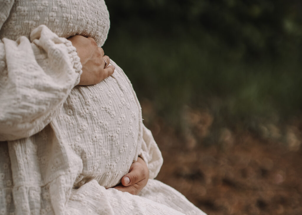 Pregnant woman holding her belly. Only her torso is visible. From the side.