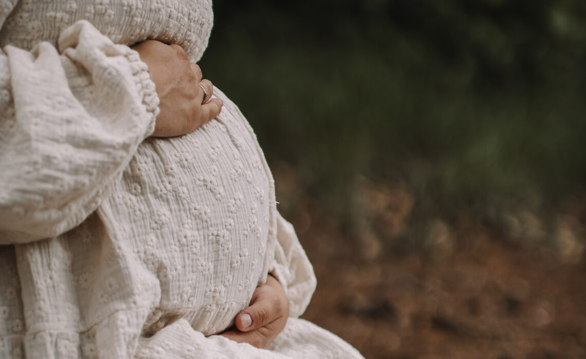 Pregnant woman holding her belly. Only her torso is visible. From the side.