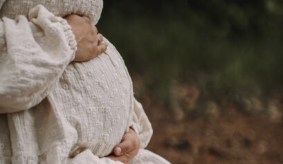 Pregnant woman holding her belly. Only her torso is visible. From the side.